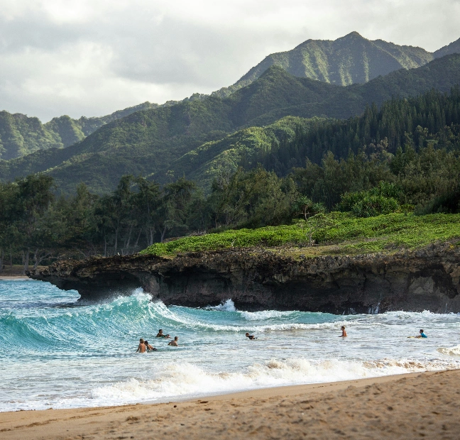 Beach with ocean waves and green mountains in the background.